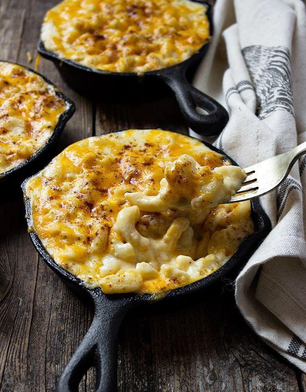 Two small cast iron skillets of creamy mac and cheese dusted with paprika, a fork lifting from the front one