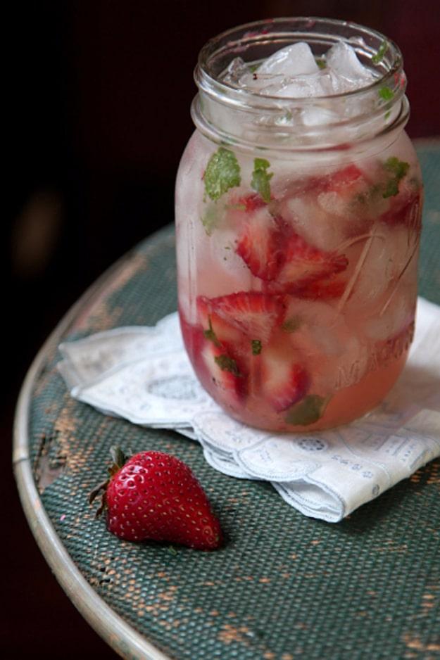 Strawberry moonshine julep in a jar packed with ice, mint leaves and sliced strawberries on a metal table