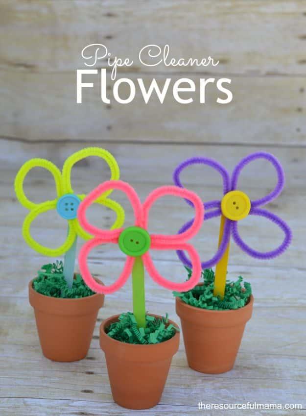 Three pipe cleaner flowers with button centers on painted popsicle stick stems, in small terracotta pots