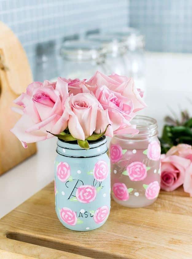 Painted rose mason jars in pale blue and grey with hand painted pink roses and white dots holding fresh roses