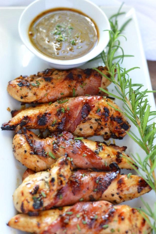 Grilled bacon wrapped chicken with cracked black pepper and rosemary sprigs on a hot grill grate for a backyard BBQ