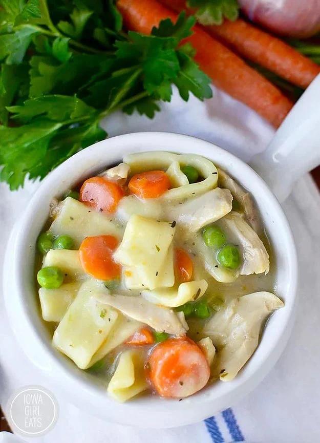 Gluten free chicken and noodles in a white bowl with wide egg noodles, carrots and peas in a creamy broth