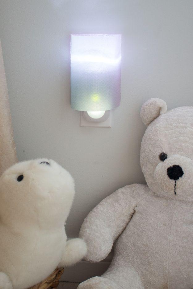 Small glowing nightlight shade made from patterned resin paper plugged into a wall beside two teddy bears
