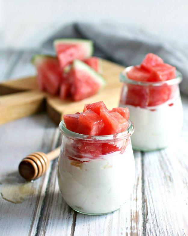 Honey drizzled watermelon and yogurt parfait layered in small glass jars with a honey dipper beside them