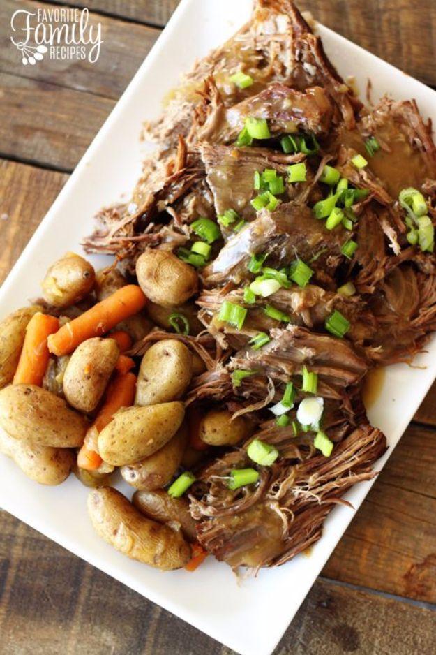 White platter of shredded pot roast with baby potatoes, carrots and gravy scattered with sliced green onions