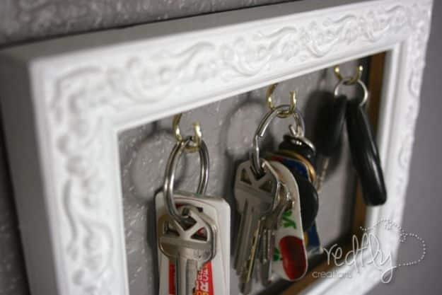 Key frame, a small ornate white picture frame hung on a grey wall, with gold hooks inside holding sets of keys