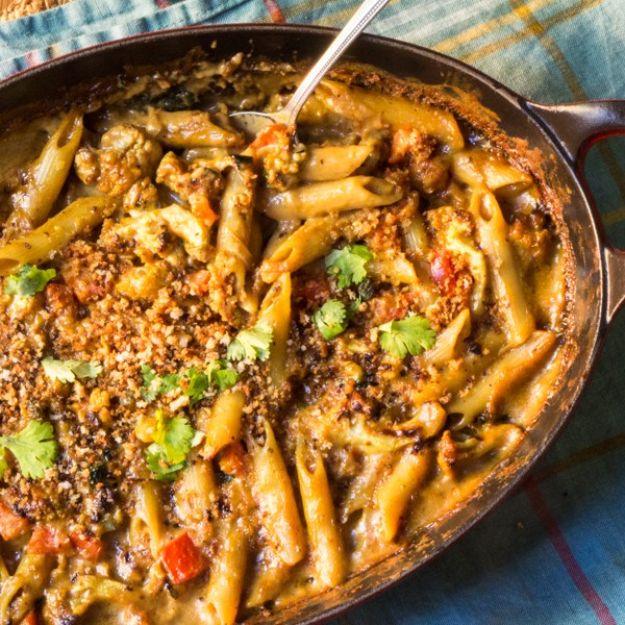 Curried cauliflower mac and cheese in a skillet with penne, toasted breadcrumbs, greens and chopped cilantro