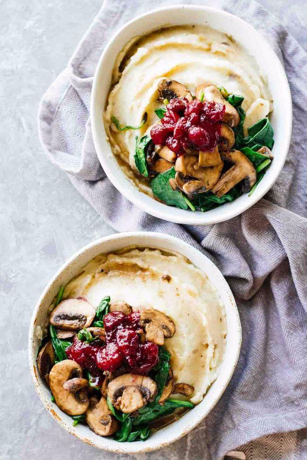 Slow cooker mashed potatoes in two white dishes topped with sauteed mushrooms, spinach and cranberry sauce