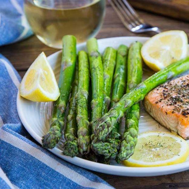 Grilled asparagus on a white plate beside a salmon fillet and lemon wedges, spears dusted with paprika