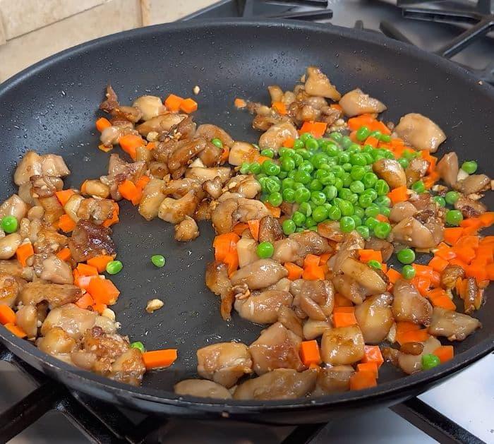 Cooking chicken, green peas, and carrots in a pan