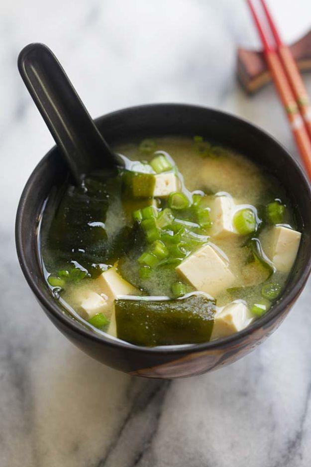 Miso soup in a dark brown bowl with silken tofu cubes, wakame seaweed, sliced scallions and a black spoon