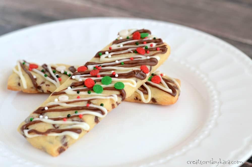 Two chocolate chip cookie sticks drizzled in zigzags of dark and white chocolate with red and green sprinkles on a plate