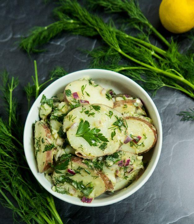 Lemon dill potato salad in a white bowl with sliced red potatoes, chopped herbs and fresh dill fronds beside
