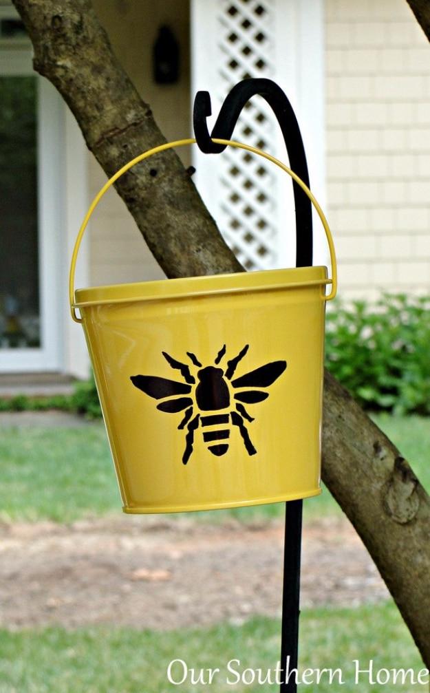 Sharpie embellished citronella bucket, a yellow metal bucket with a black bee design hanging from a shepherd hook