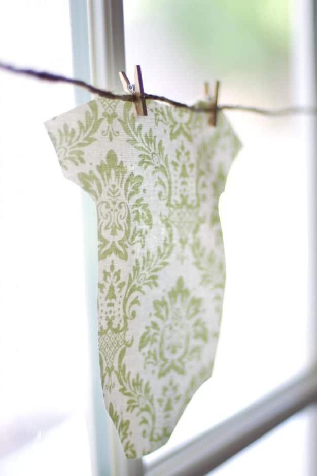 DIY baby shower decoration with a green damask print fabric onesie pegged to twine with wooden clothespins by a window
