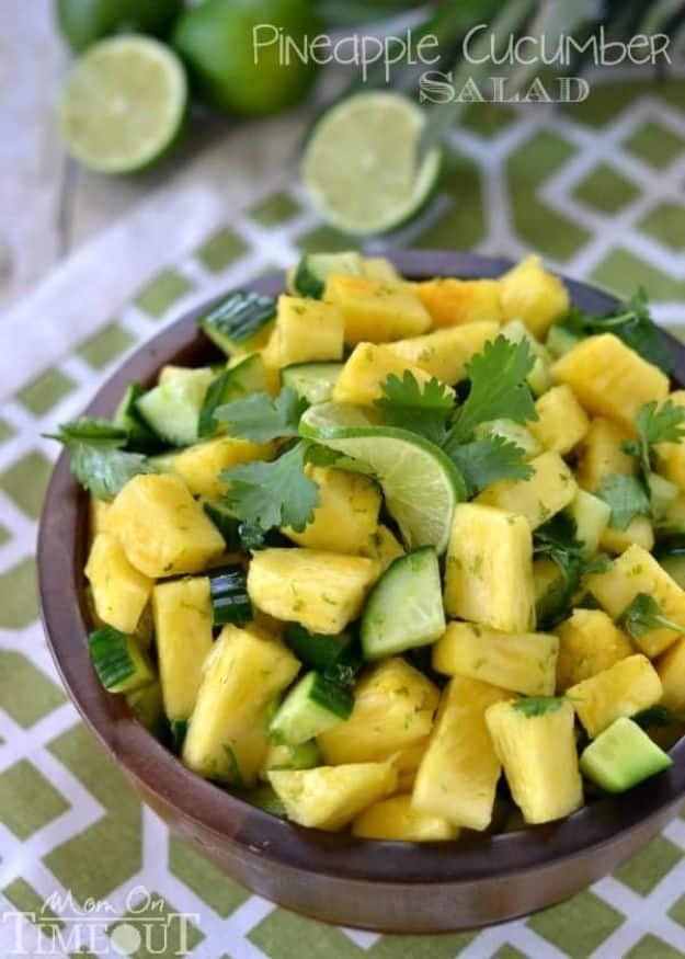 Pineapple cucumber salad in a wooden bowl with chopped pineapple, cucumber, cilantro and lime halves beside