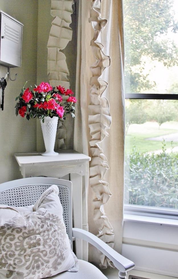 Cream drop cloth curtain panel with a deep vertical column of ruffles, beside a white table and a cane chair
