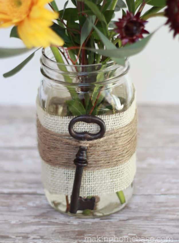 Mason jar wrapped in burlap and jute with a black skeleton key charm, holding yellow and burgundy flowers