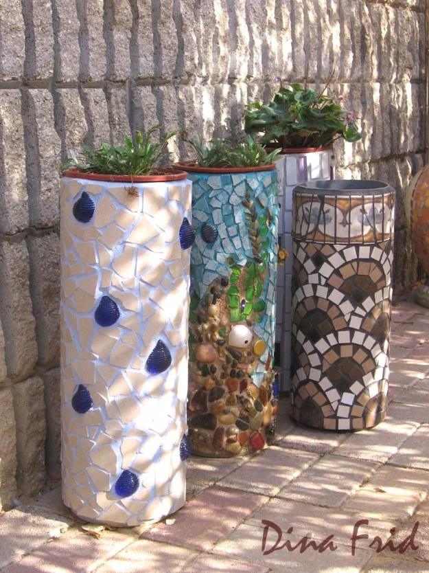 PVC pipe planters, three tall mosaic covered columns in white, blue and brown tile holding green plants against a stone wall
