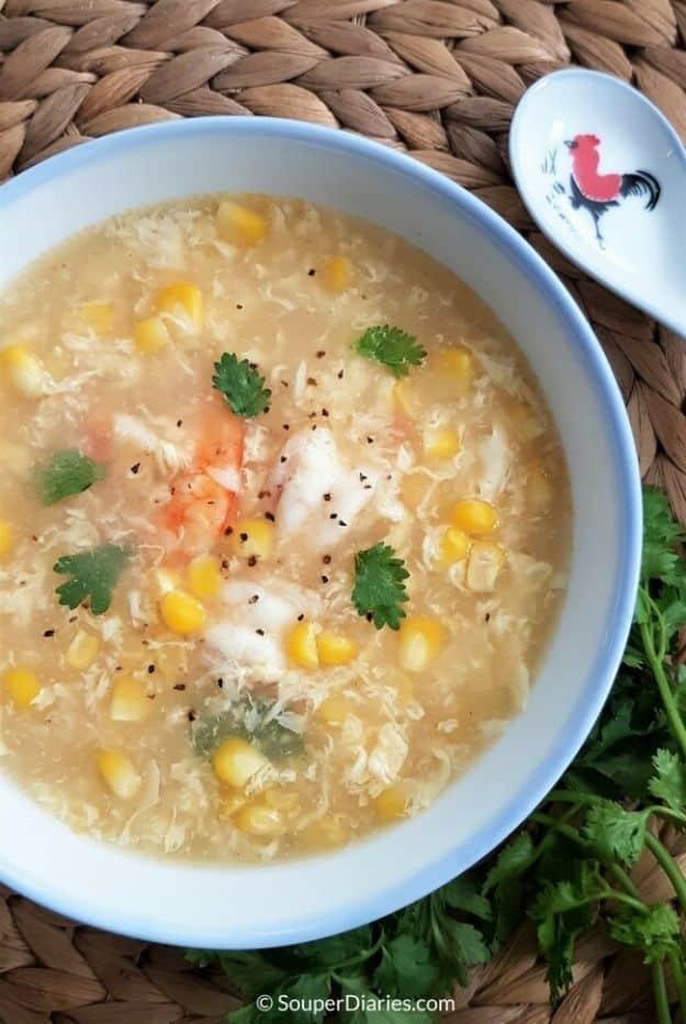 Shrimp egg drop soup in a pale blue bowl with corn kernels, whole shrimp, egg ribbons and cilantro leaves