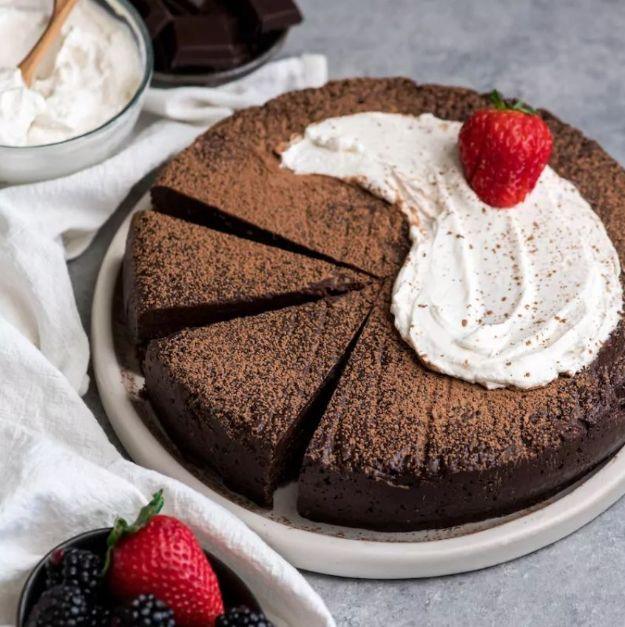 Flourless chocolate truffle cake dusted with cocoa, part sliced, with whipped cream and a strawberry on top