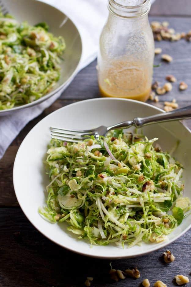 Shaved brussels sprout salad with toasted walnuts and red onion in a white bowl beside a dressing jar