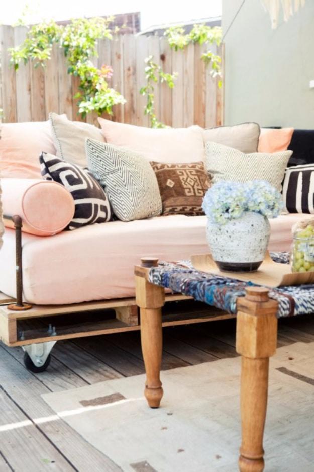 Pallet outdoor daybed on castors with a blush mattress, black and white pillows and peach bolsters on a wooden deck