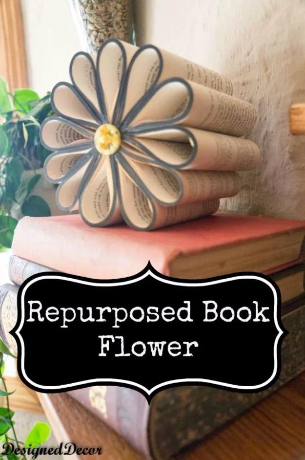 Repurposed book flower graphic, a cut book fanned into petals with a yellow button center, on a stack of books