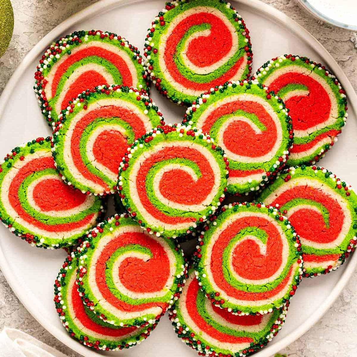 Red, white and green pinwheel cookies with a spiral swirl and a border of holiday nonpareils arranged on a white plate