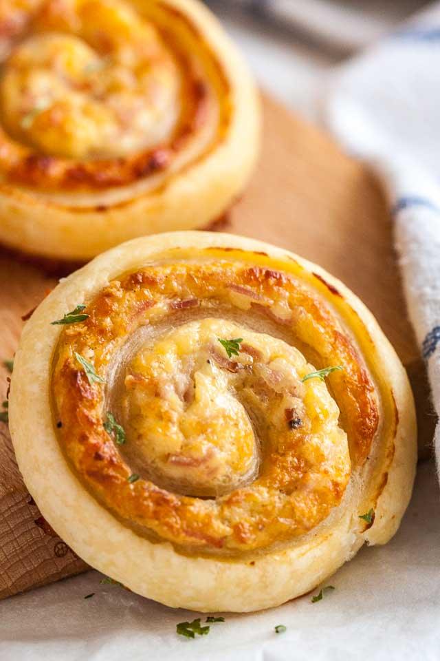 Ham and cheese pinwheels made with puff pastry, baked golden with melted cheese, on a wooden serving board