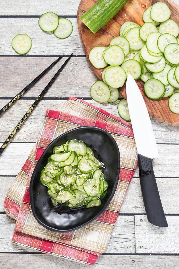 Japanese cucumber salad in a black dish with paper thin cucumber slices, beside a knife and sliced cucumber