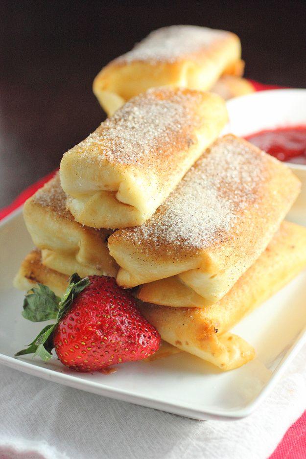 Fried cheesecake rolls dusted with cinnamon sugar, stacked high on a white plate beside a fresh strawberry