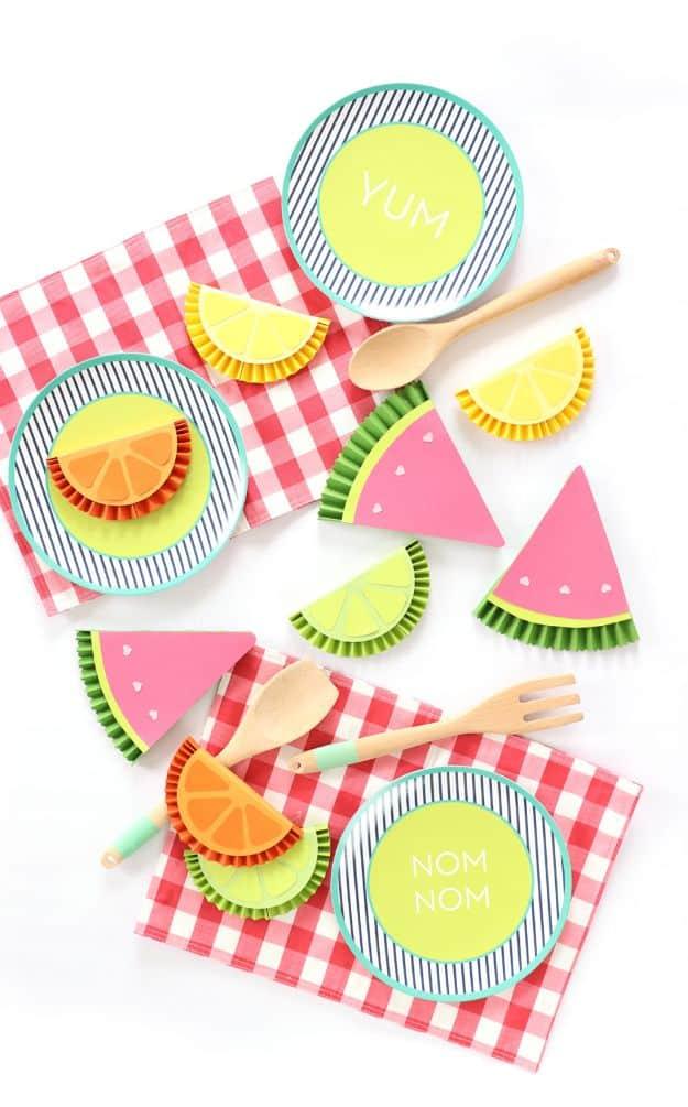 Paper citrus slices and watermelon wedges with paper plates and wooden cutlery on red gingham picnic napkins