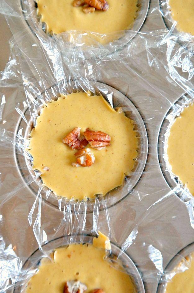 Mini vegan pumpkin pie cheesecakes with pecan date crusts, set in a muffin tin and topped with pecan halves