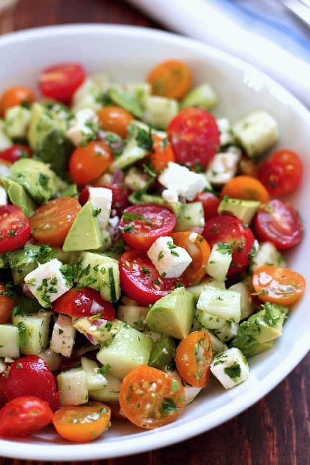 Tomato cucumber avocado salad in a white bowl with cherry tomatoes, cucumber, avocado and cubed feta cheese