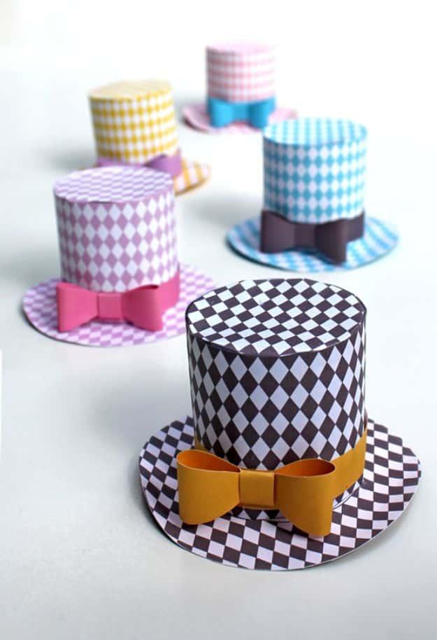 Five printed paper mini top hats in harlequin patterns with paper bows, arranged on a plain white surface