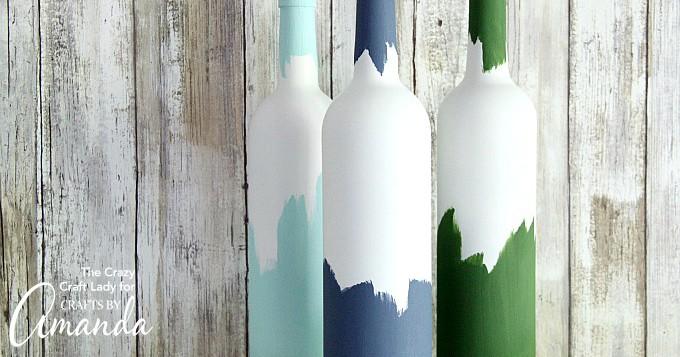 Painted wine bottles, three white bottles dipped in mint, navy and dark green with ragged edges on whitewashed wood