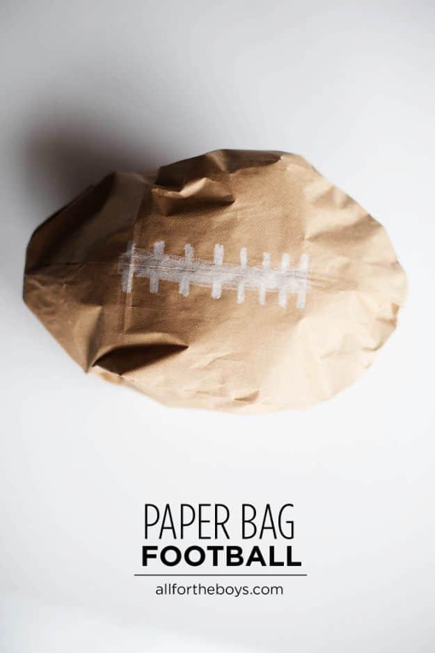 Brown paper bag football with white crayon laces on a plain white surface, under a typeset Paper Bag Football title