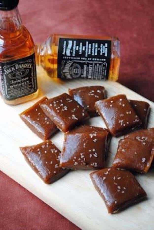 Salted whisky caramels cut into squares and dusted with flaked sea salt beside miniature whiskey bottles