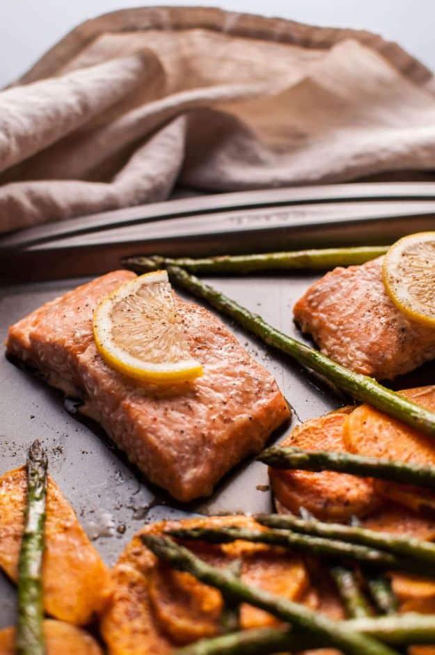Maple salmon sheet pan dinner with two salmon fillets, lemon slices, asparagus and sweet potato on a dark pan