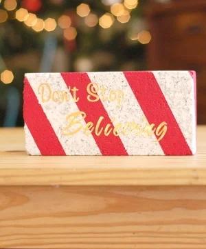 Brick painted white with red candy cane stripes and gold Don't Stop Believing lettering, lit by Christmas lights