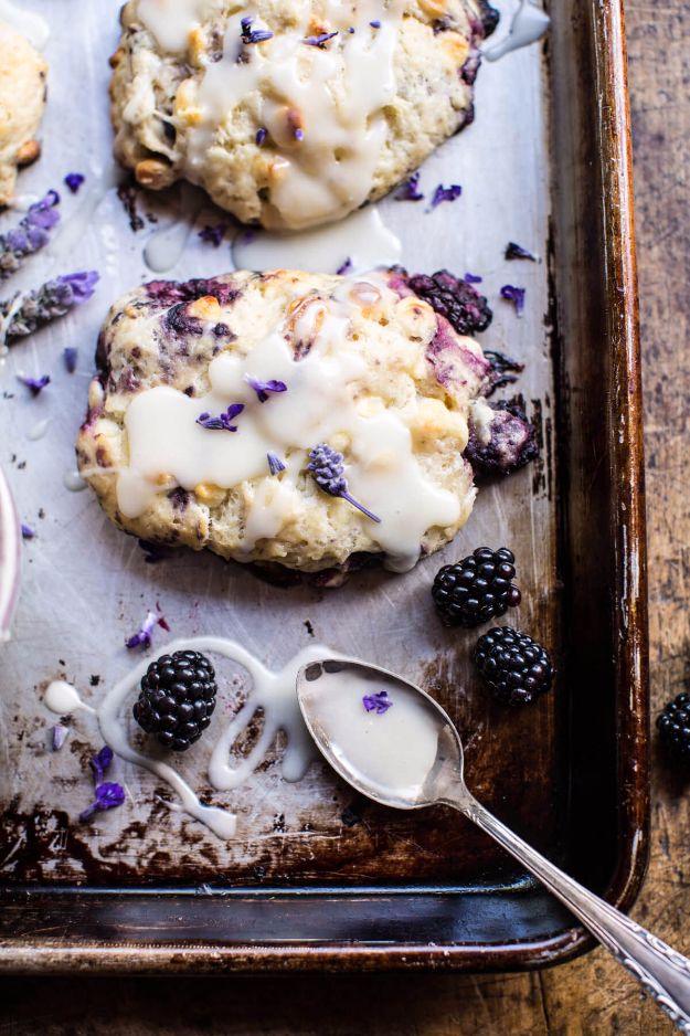Baking sheet of blackberry scones with white glaze and lavender buds, a glazed spoon and loose berries