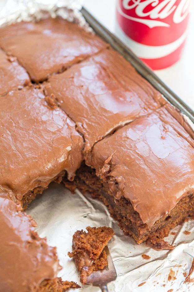 Coca Cola cake in a foil lined 9x13 pan under thick glossy chocolate frosting, cut into squares, with a Coke can behind
