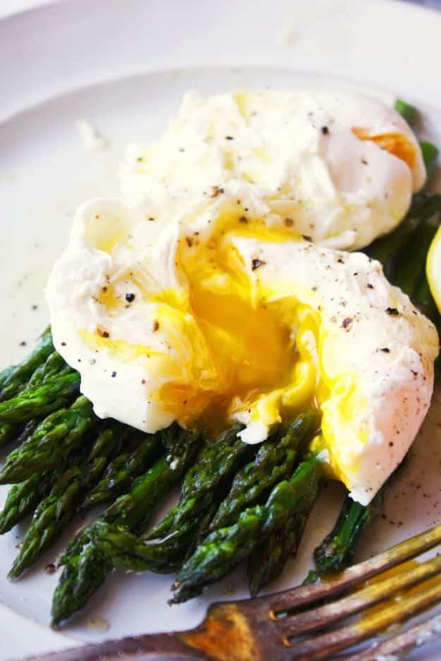 Poached eggs over roasted asparagus on a white plate, broken yolk running over green spears with pepper