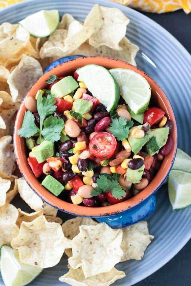 Mexican bean dip with black beans, corn, tomatoes and avocado in a terracotta bowl with tortilla chips and lime