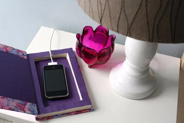 DIY cell phone charging book with a purple floral hardcover open on a nightstand holding a phone and its cord
