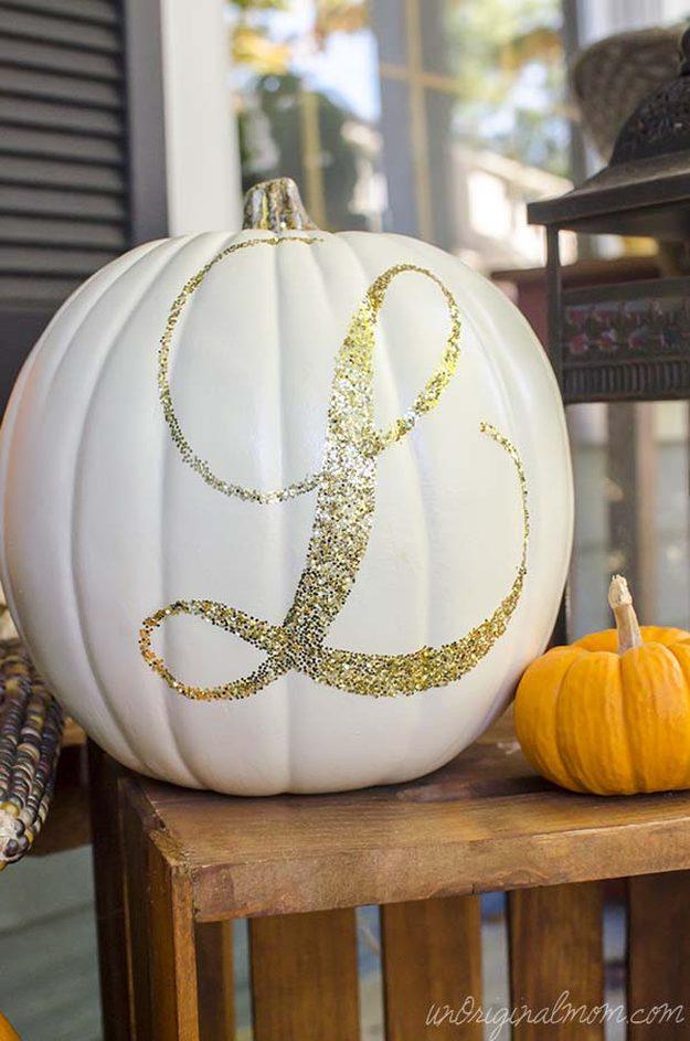 White craft pumpkin with a large gold glitter cursive letter L on a wood crate beside a small orange pumpkin