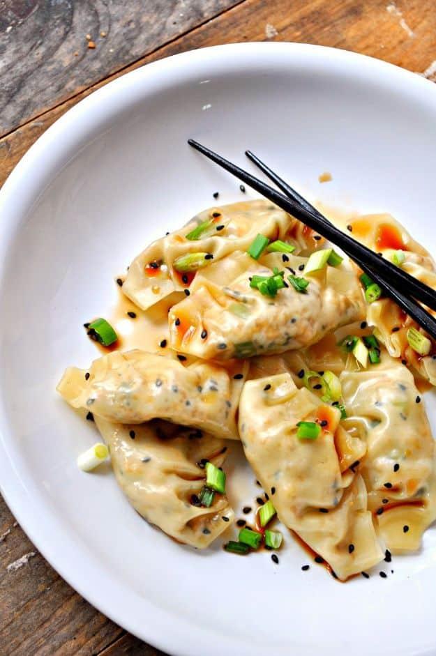 Vegan sesame tofu dumplings on a white plate with chopsticks, chili oil, green onion and black sesame seeds