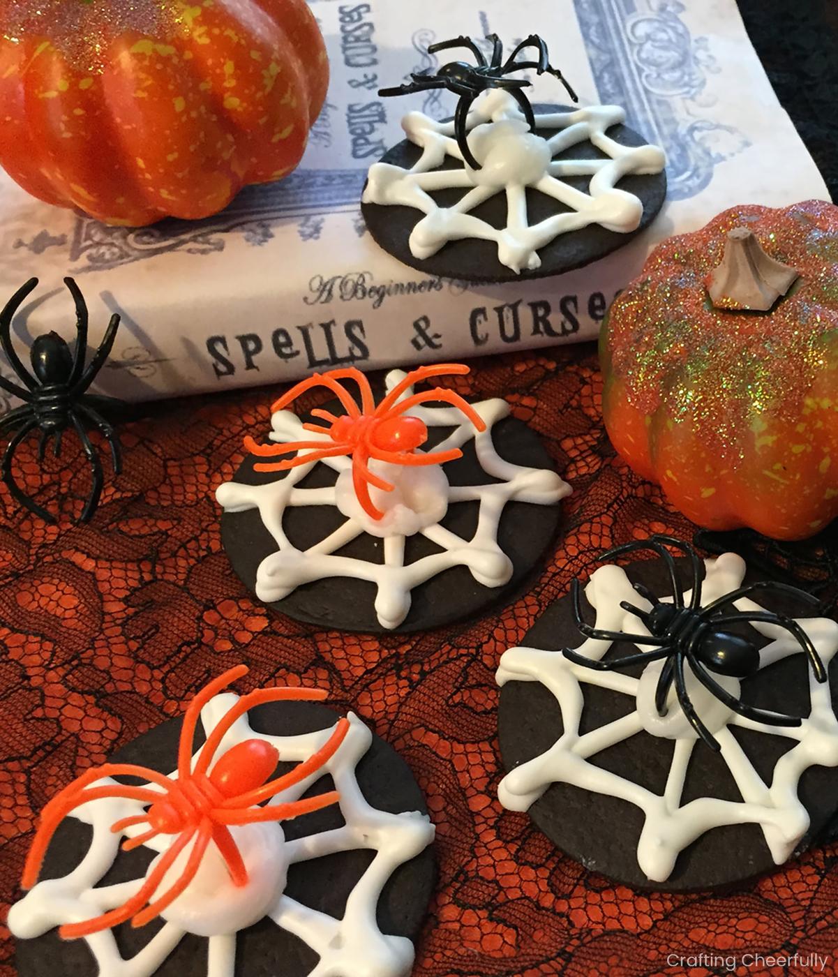 Chocolate wafer cookies with white piped spiderwebs and removable plastic spider rings on a Halloween platter