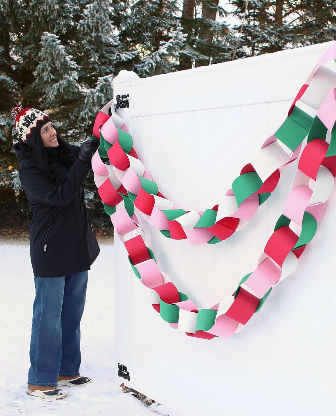 Giant chunky paper chain in pink, red, green and white craft foam swagged across a white gate in a snowy yard